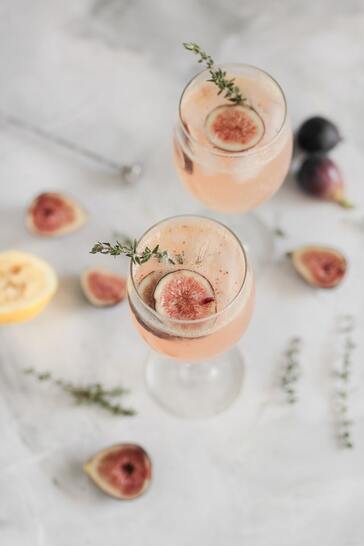 Pink cocktail in wine glass with herb and fruit garnish